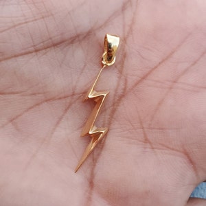 May include: A gold-colored lightning bolt pendant charm. The pendant is made of metal and has a smooth, polished finish.