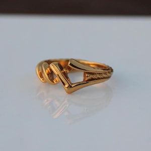 May include: A gold ring with a unique, abstract design. The ring is made of a thick, textured metal and has a geometric shape.