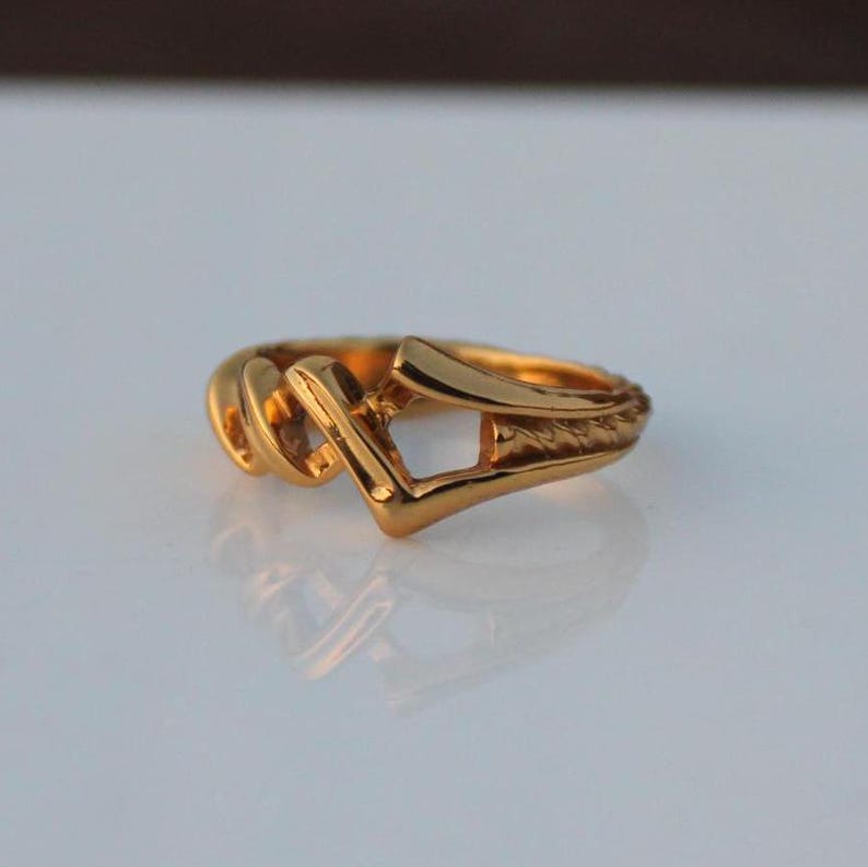 May include: A gold ring with a unique, abstract design. The ring is made of a thick, textured metal and has a geometric shape.