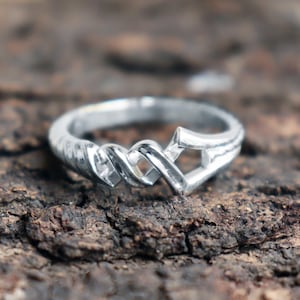May include: A silver ring with a twisted, interwoven design. The ring is made of a smooth, polished metal and has a simple, elegant style.