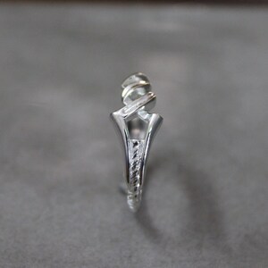 May include: A silver ring with a unique, twisted design. The band is textured and the top of the ring is open.