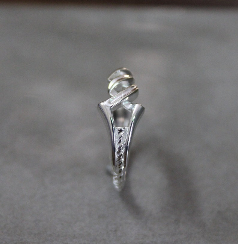 May include: A silver ring with a unique, twisted design. The band is textured and the top of the ring is open.