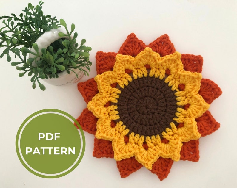 May include: Crochet sunflower coaster pattern in PDF format. The coaster is made with orange, yellow, and brown yarn. The pattern includes instructions for creating the sunflower petals, center, and backing.