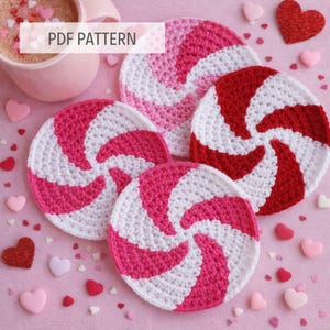 May include: Handmade crochet coasters in a spiral design, in shades of pink, red, and white. The coasters are arranged on a pink surface with heart-shaped decorations and a coffee cup. The text "PDF PATTERN" is visible.
