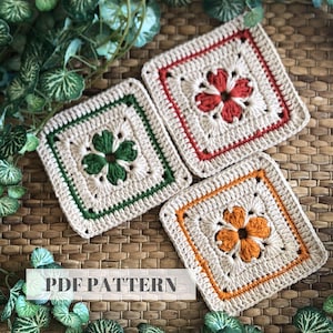 Può includere: Tre sottobicchieri quadrati all'uncinetto in crema, con disegni floreali in verde, rosso e arancione. Ogni sottobicchiere ha un bordo colorato e un fiore centrale. Il testo "PDF PATTERN" è visibile in basso.