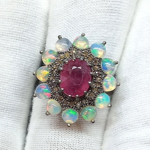 May include: A silver ring with a large pink oval gemstone surrounded by smaller white opals and diamonds.
