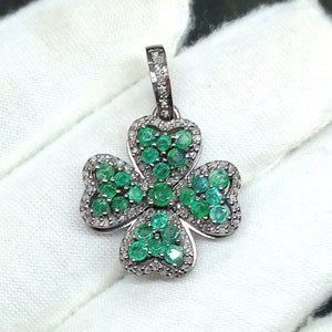 May include: A silver four-leaf clover pendant set with green emerald gemstones and white diamonds.