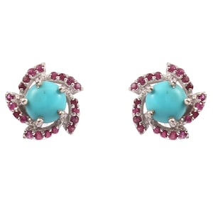 Könnte beinhalten: Ein Paar Ohrstecker mit einem zentralen türkisfarbenen Stein, umgeben von kleinen, runden, roten Edelsteinen. Die Ohrringe haben ein florales Design und sind in einem silberfarbenen Metall gefasst.