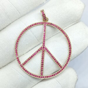 May include: A gold peace sign pendant with a red ruby stone outline. The pendant is set with small red ruby stones.