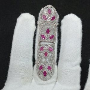 May include: A silver ring with a delicate filigree design and pink gemstones. The ring is designed to be worn on the middle finger.