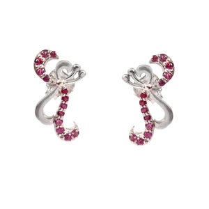 May include: A pair of silver stud earrings. Each earring has a curved design with a line of small, round, red gemstones. The earrings have a delicate, elegant appearance, suitable for formal or everyday wear.
