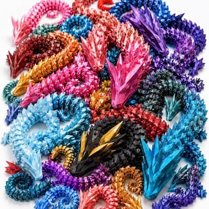 Könnte beinhalten: Eine Sammlung von beweglichen Drachenfiguren mit einem geometrischen, facettierten Design. Die Drachen sind in einer Vielzahl von metallischen und soliden Farben gehalten, darunter Pink, Blau, Lila, Gold, Schwarz, Rot und Türkis, dicht angeordnet.