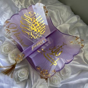 Peut inclure: Un plateau en résine en forme de papillon violet avec des accents de feuilles d'or et de la calligraphie arabe en or. Le plateau est décoré de paillettes dorées et est accompagné d'un marque-page assorti avec un pompon.