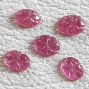 May include: Five oval pink gemstones with carved floral patterns. The gemstones are a vibrant pink colour and appear polished. The carvings are detailed, adding texture to the smooth surface of the stones.