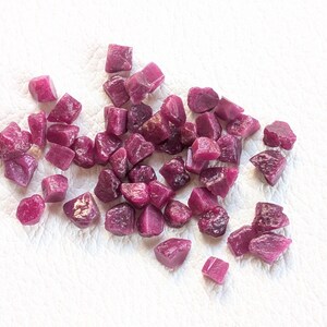 Peut inclure: Un ensemble de pierres précieuses de rubis brutes et non taillées. Les pierres sont d'un rouge profond et riche, avec une surface légèrement rugueuse et texturée. Les pierres sont disposées sur une surface blanche.