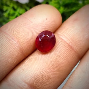 May include: A deep red oval-shaped gemstone with a faceted cut.