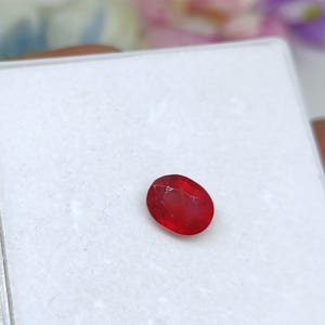May include: A bright red oval gemstone on a white background.