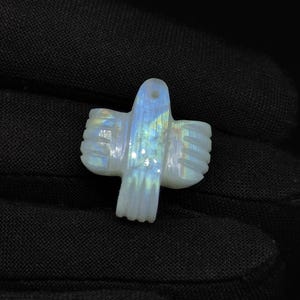 May include: A white iridescent moonstone pendant carved in the shape of a bird. The pendant has a hole at the top for attaching a chain.