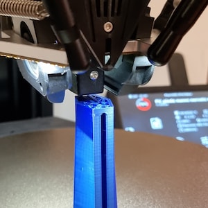 May include: A 3D printed blue object with a long, thin slot running down the center. The object is being printed by a 3D printer.