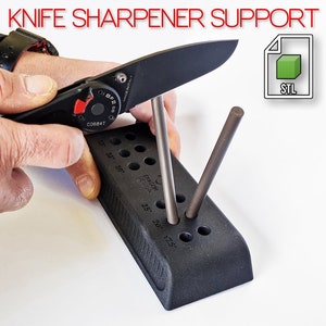 Può includere: Un supporto per affilare i coltelli nero con una varietà di fori di diverse dimensioni per affilare i coltelli. Il supporto è in plastica e ha una superficie testurizzata. Il supporto viene utilizzato per affilare un coltello pieghevole nero. L'immagine include anche un'icona di file di modello 3D con il testo "STL".