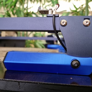 May include: A close-up of a blue 3D printed part with a black screw on the side. The part is attached to a black metal frame with two silver screws.