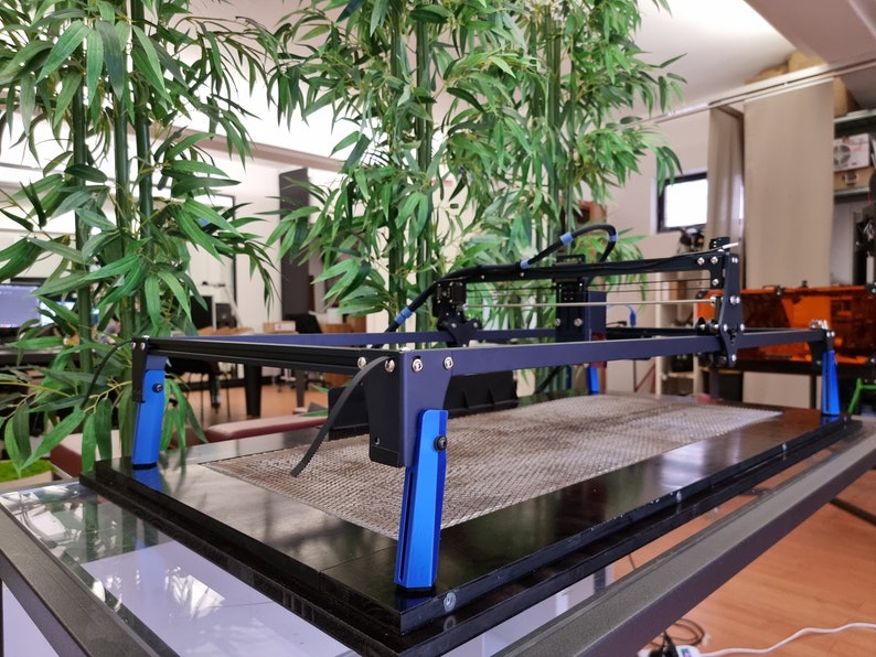 May include: A black 3D printer with a blue frame and blue supports. The printer is on a glass table with a black surface.