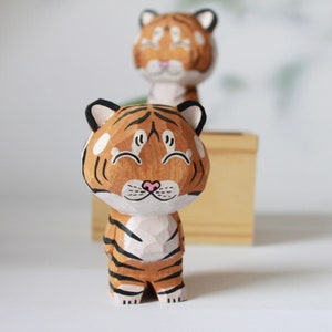 Może przedstawiać: Drewniana rzeźba tygrysa z czarnymi paskami i różowym nosem. Tygrys ma szczęśliwy wyraz twarzy z zamkniętymi oczami i szerokim uśmiechem.