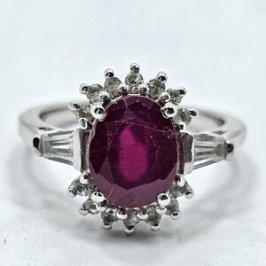 Puede incluir: Un anillo de plata con una gran gema de rub&iacute; de corte ovalado y piedras de acento m&aacute;s peque&ntilde;as. El rub&iacute; es de color rojo intenso, y las piedras de acento son claras. El anillo tiene un dise&ntilde;o cl&aacute;sico y elegante.