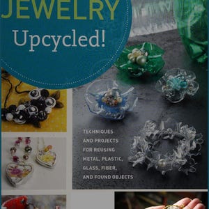 May include: A book cover with the title "Jewelry Upcycled!" and a colourful collage of jewellery made from recycled materials. The book cover features techniques and projects for reusing metal, plastic, glass, fibre, and found objects.