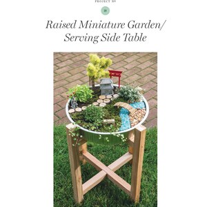 May include: A raised miniature garden in a white container, featuring a miniature Japanese-style landscape with a bridge, miniature trees, and a small pagoda. The container sits on a wooden stand. Text on the page reads "Raised Miniature Garden/ Serving Side Table".