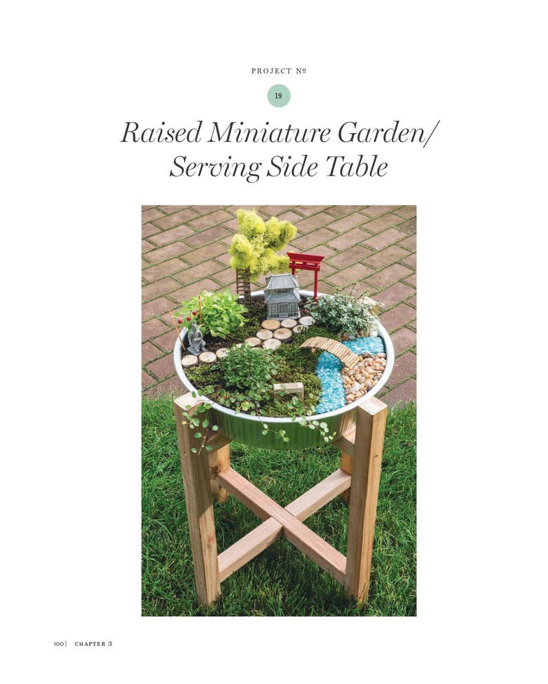 May include: A raised miniature garden in a white container, featuring a miniature Japanese-style landscape with a bridge, miniature trees, and a small pagoda. The container sits on a wooden stand. Text on the page reads "Raised Miniature Garden/ Serving Side Table".