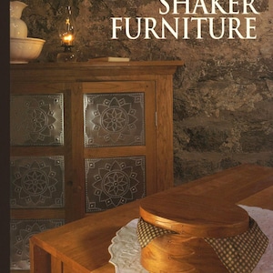 Może przedstawiać: Książka zatytułowana "The Art of Woodworking Shaker Furniture" ze zdjęciem drewnianej szafki z blaszanymi panelami i drewnianego stołu z drewnianym pudełkiem na górze.