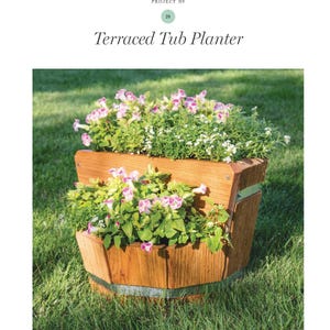 May include: A terraced tub planter made of wood, filled with vibrant green plants and pink and white flowers. The planter has a rustic design with metal bands and is set on a grassy lawn. The text "Terraced Tub Planter" is at the top.