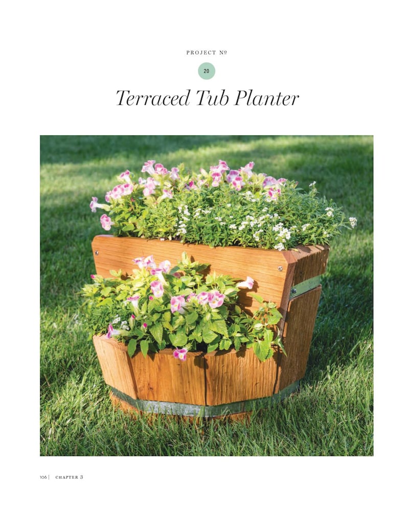 May include: A terraced tub planter made of wood, filled with vibrant green plants and pink and white flowers. The planter has a rustic design with metal bands and is set on a grassy lawn. The text "Terraced Tub Planter" is at the top.