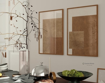 May include: Two framed abstract art prints with brown and beige geometric shapes hang on a light-colored wall. A dining table is set with a gray tablecloth, a loaf of bread, and a bowl of artichokes. A tall pink vase and a silver serving dish are also on the table.