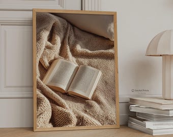 Può includere: Una stampa artistica rettangolare incorniciata che mostra un libro aperto appoggiato su una coperta in maglia beige testurizzata. La stampa è esposta in una cornice di legno chiaro, mostrando una scena con luce soffusa e toni neutri, con il testo IonArt Prints visibile.