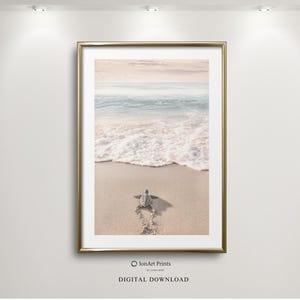 Puede incluir: Impresión enmarcada de una escena de playa con una tortuga marina dirigiéndose al mar. La obra de arte tiene un marco dorado y muestra un cielo y un océano en colores pastel. La tortuga deja un rastro en la arena.