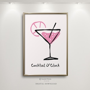 May include: A framed print featuring a pink cocktail illustration with a lime slice and a straw. The words "Cocktail O'Clock" are written below the image in black. The artwork is set against a white background.