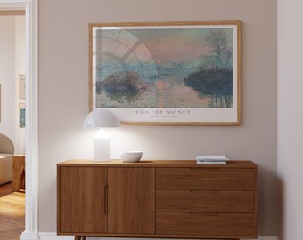 May include: A rectangular framed art print of a Claude Monet landscape painting featuring a sunrise over water, hung above a wooden sideboard with one cabinet door and three drawers. A white table lamp and a small bowl sit on the sideboard surface.