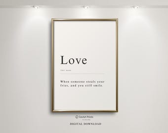 Puede incluir: Un cartel enmarcado con la palabra "Love" en negrita, en negro. Debajo, una definición dice: "Cuando alguien te roba las patatas fritas y aún sonríes". El cartel tiene un marco dorado y está contra una pared blanca.