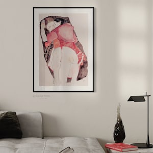 Puede incluir: Una l&aacute;mina art&iacute;stica enmarcada que muestra una ilustraci&oacute;n estilo acuarela de dos figuras abrazadas. Las figuras tienen tonos de piel p&aacute;lidos, una viste una prenda roja, sobre un fondo oscuro y abstracto dentro de un marco negro.