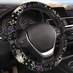May include: Black steering wheel cover featuring a skull, purple roses, and star patterns. The floral and skull design is set against a black background. The cover is designed to fit a standard car steering wheel.