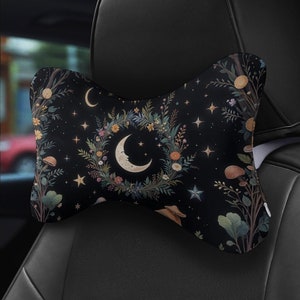 May include: A black car headrest pillow with a celestial design. The pillow features a crescent moon, stars, and a floral wreath on a dark background. The design includes mushrooms and various plants.