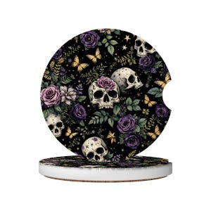 May include: A round car coaster with a black background featuring a floral and skull design. The design includes purple roses, butterflies, and skulls with rose accents. The coaster sits on a white and brown base.