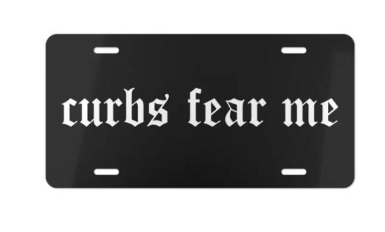 Puede incluir: Placa de matr&iacute;cula negra con la frase "curbs fear me" en fuente g&oacute;tica blanca. La placa tiene cuatro orificios de montaje y un acabado brillante. Un accesorio llamativo.