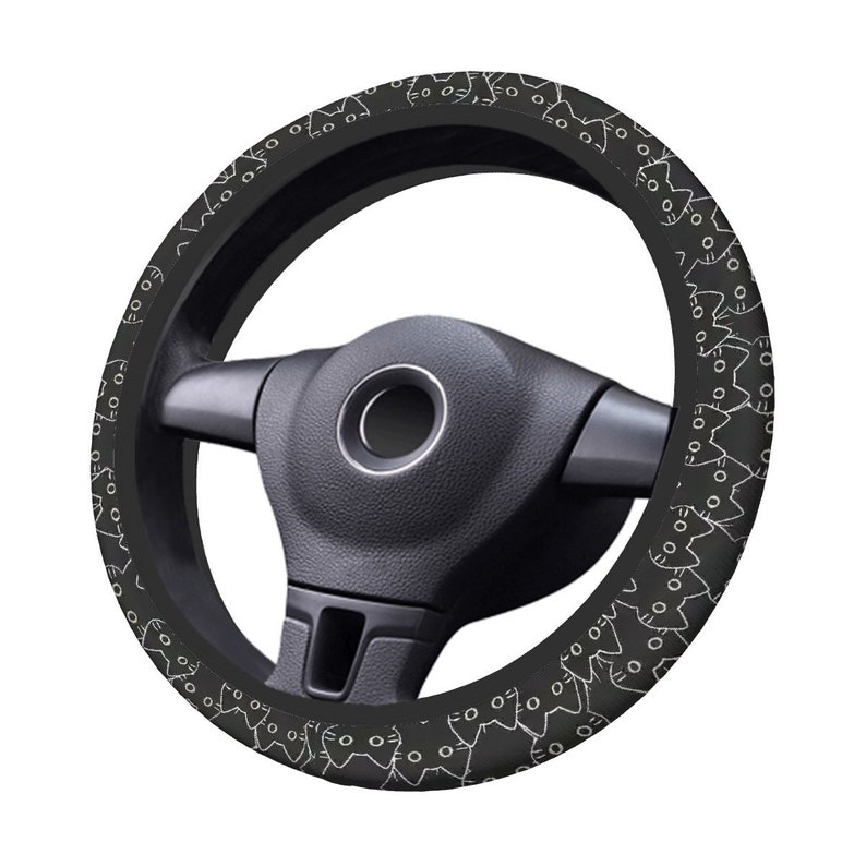 May include: Black steering wheel cover featuring a white cat pattern. The cover is designed to fit a standard steering wheel. The cat design is repeated around the entire cover. The steering wheel is black.