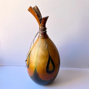 Op de afbeelding: Een handgemaakte kalebasvaas met een druppelvorm. De vaas heeft een natuurlijke bruine kleur met donkergroene en zwarte geschilderde accenten. De bovenkant heeft een uniek, gespleten ontwerp en is omwikkeld met draad en touw.