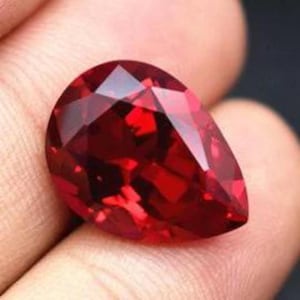 Puede incluir: Una gran gema roja en forma de pera con muchas facetas.