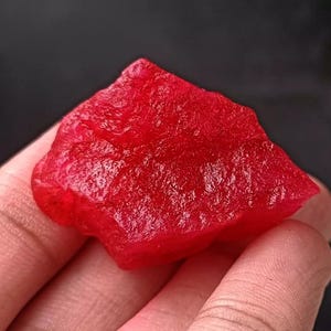 May include: A large, rough, red gemstone with a deep, rich colour. The gemstone has a natural, unpolished surface.