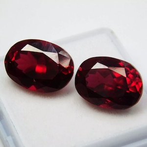 May include: Two oval-shaped, deep red gemstones with a faceted cut.